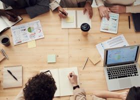 Business professionals in a collaborative team meeting, discussing charts and plans with laptops and notebooks.